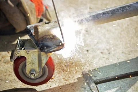 Worker with a welding machine fixing a caster wheels, sparks flying around Stock Photos
