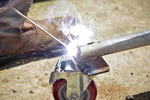 Worker with a welding machine fixing a caster wheels, sparks flying around Foto stock