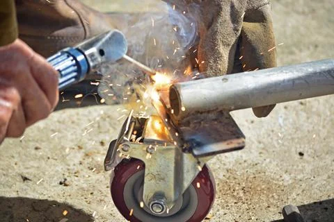 Worker with a welding machine fixing a caster wheels, sparks flying around Stock Photos