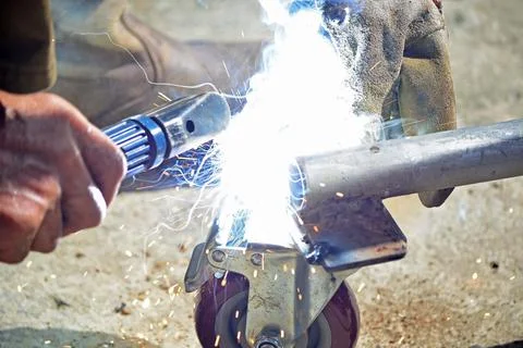 Worker with a welding machine fixing a caster wheels, sparks flying around Stock Photos