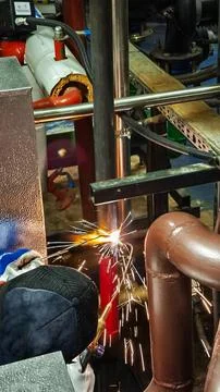 Worker welding metal pipe with torch sparks in technical room Stock Photos