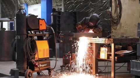 A worker welds metal structures at a factory, standing behind a workbench Stock Footage 304128742