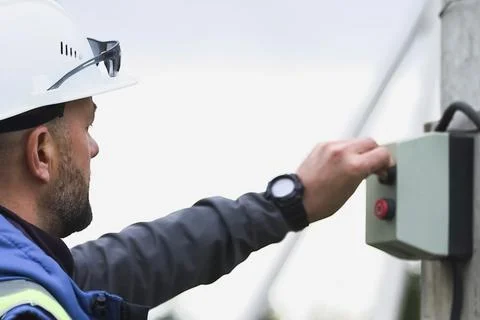Worker in a white helmet presses the start button on a box with buttons. Stock Photos