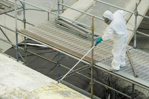 A worker in a white protective suit and mask is carefully spraying a coating  Stock Photos