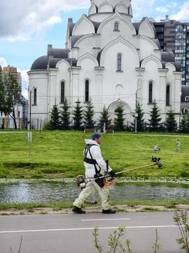 Worker in a white protective suit uses a brush cutter 写真素材