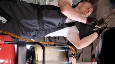 A worker working under a car changes the engine oil. A car mechanic works at a Stock Footage 250026556