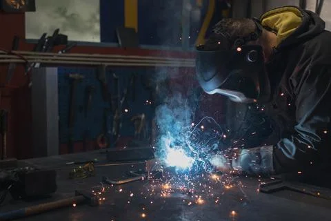 Worker working in a workshop creating sparks while welding metal materials Stock Photos