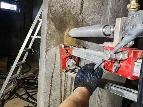 A worker works with a diamond drill on a machine fixed to the wall, drills a Stock Photos