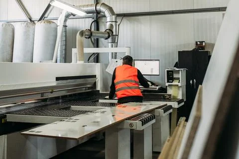 A worker works on a modern machine for cutting slabs of furniture fittings. Stock Photos