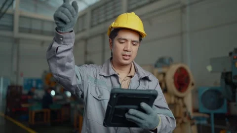 Worker in yellow hard hat uses tablet in factory Stock Footage 338432781