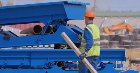 A worker in a yellow vest and orange helmet helps a crane to lay down parts Stock Footage 161963335