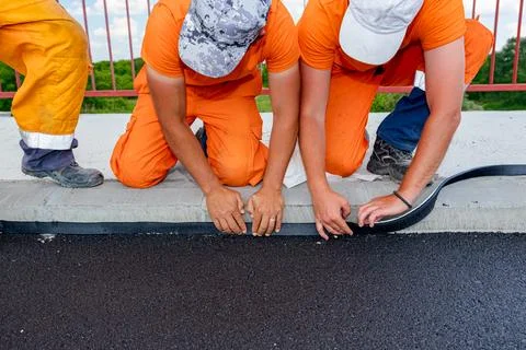 Workers apply black bitumen membrane strips for waterproofing roads Stock Photos