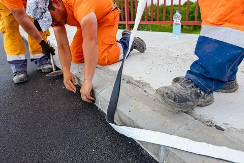 Workers apply black bitumen membrane strips for waterproofing roads Stock Photos