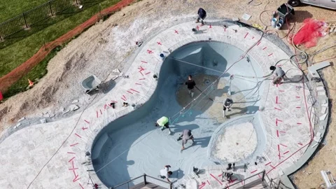 Workers apply pebble finish to curved pool shell during construction at private Stock Footage 340042420