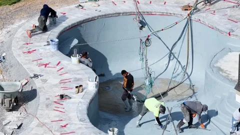 Workers apply pebble sheen finish inside freshly plastered swimming pool Stock Footage 339034832
