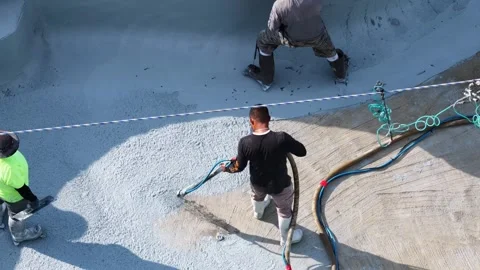 Workers apply pebble sheen finish inside curved swimming pool, hoses, sprayer Vídeos de archivo 339072506