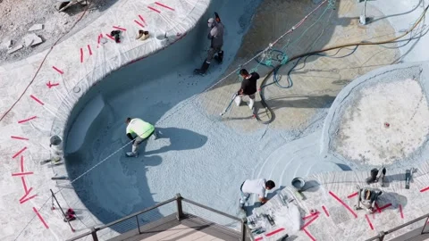 Workers apply pebble sheen finish inside curved swimming pool, spraying blue Stock Footage 339111261