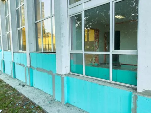 Workers are applying blue insulation around the base of a building. Windows a Stock Photos