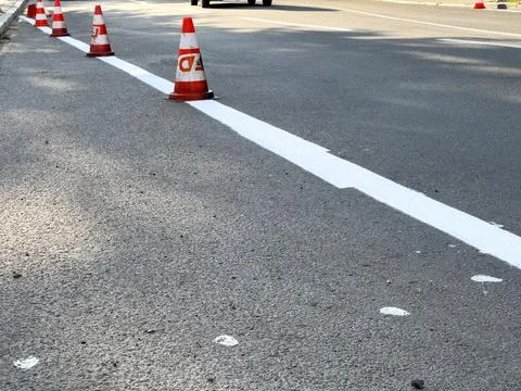 Workers are applying fresh white paint on a city road while traffic cones e.. Stock Photos