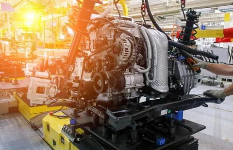 Workers are assembling an automotive engine on a conveyor system in a well-li Stock Photos