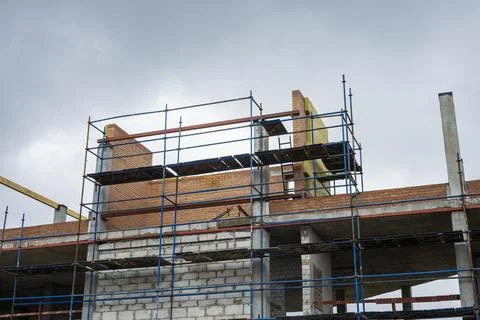 Workers are building a structure with brick walls and scaffolding. The sky is Photos
