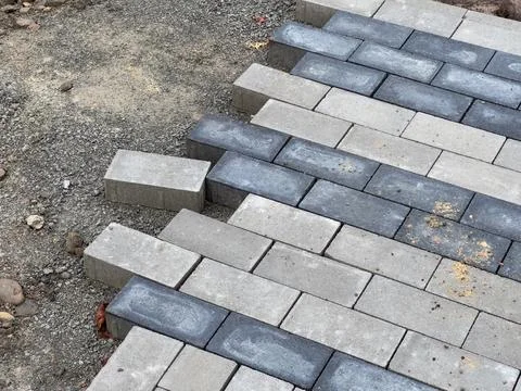 Workers are carefully laying down paving stones on a gravel foundation. Stock Photos