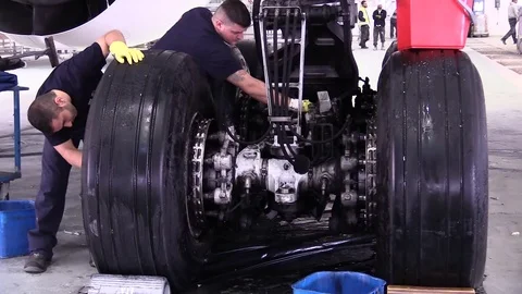 Workers are cleaning in detail huge wheels of a plane inside the hangar Stock Footage 88504591
