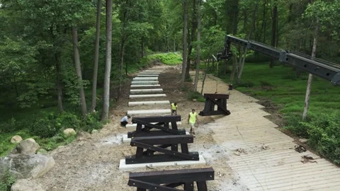 Workers are constructing a wooden walkway in a forest area. A crane is lifting Stock Footage 328072345