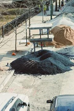 Workers are engaged in construction activities near a sidewalk. There are lar Stock Photos