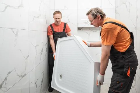 Workers are installing a shower tray in the bathroom. Stock Photos