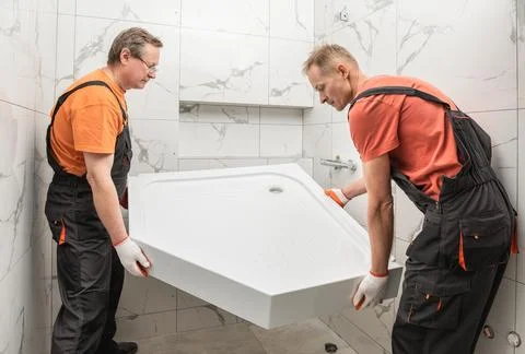Workers are installing a shower tray in the bathroom. Stock Photos