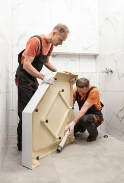 Workers are installing a shower tray in the bathroom. Stock Photos