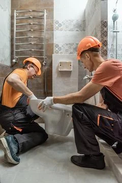 Workers are installing a wall-hung toilet on the wall. Stock Photos