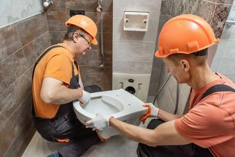 Workers are installing a wall-hung toilet on the wall. Stock Photos