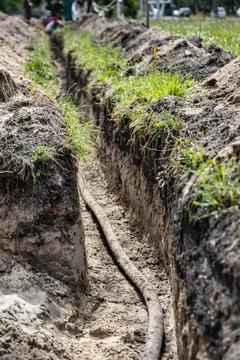 Workers are laying a high voltage cable in a trench at a construction site, w Stock Photos