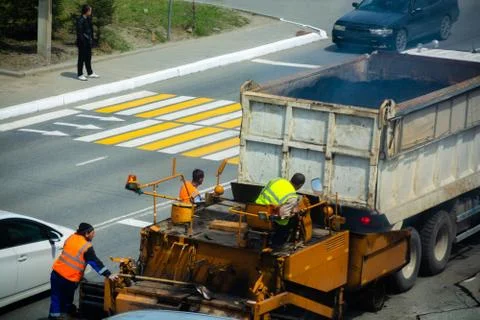 Workers are loading asphalt in the paver. Road construction. Asphalt paving. Stock Photos