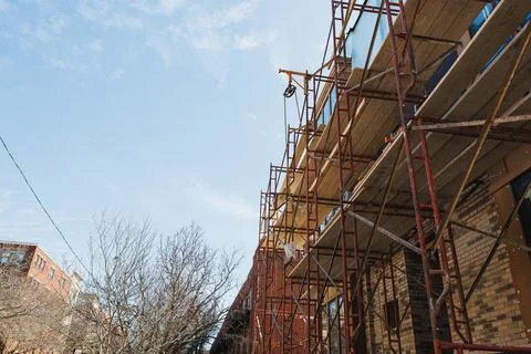 Workers are performing construction tasks on a building which has scaffolding Stockfoto's