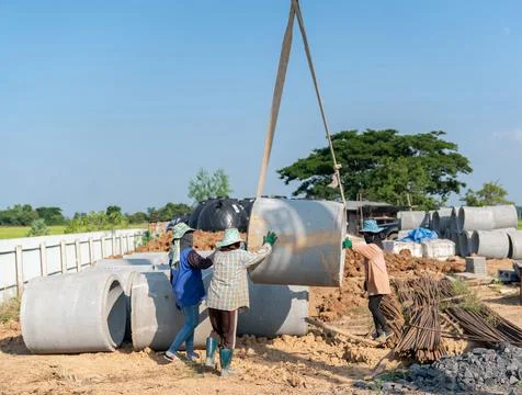 Workers are sorting large concrete pipes at a construction site. Stock Photos