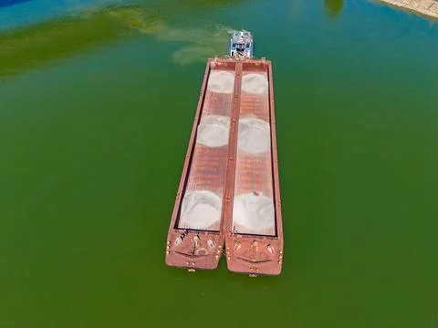 Workers are on top of a large cargo barge that is floating on green water. Th Stock Photos