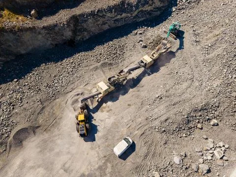 Workers are using heavy machinery to extract granite in a quarry. Trucks are  Stock Photos