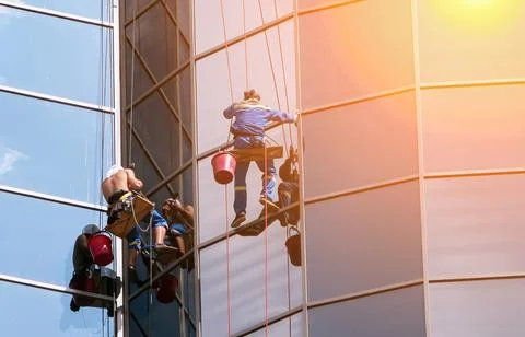 Workers are using ropes and buckets to wash the windows of a tall building in Stock Photos