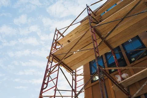 Workers are using scaffolding to access a tall structure. The sky is clear wi Stock Photos