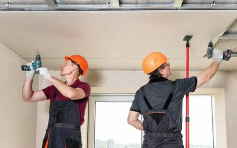 Workers are using screws and a screwdriver to attach plasterboard to the ceil Stock Photos