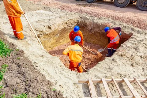 Workers are using shovels for realign excess of ground to correct trench meas Stock Photos