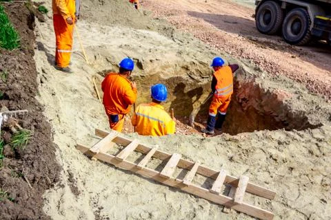 Workers are using shovels to set up right measures in square trench Stock Photos