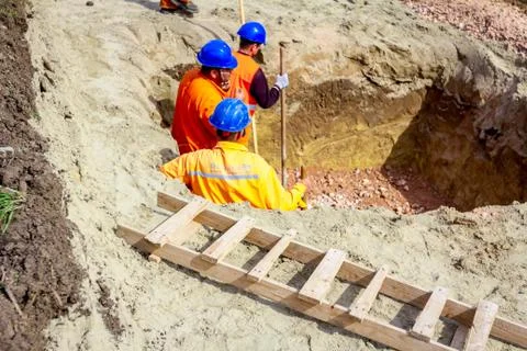 Workers are using shovels to set up right measures in square trench Stock Photos
