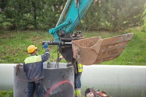 Workers are working on the construction site. An excavator uses a chain to lift Stock Photos