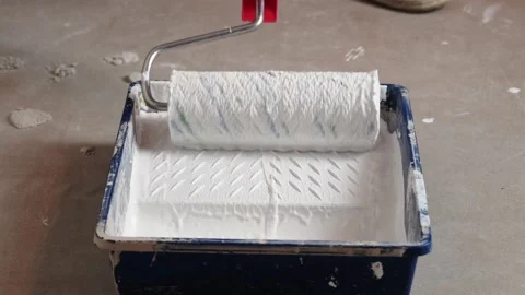 The worker's arm dips the roller into white paint to paint the wall Stock Footage 145572794