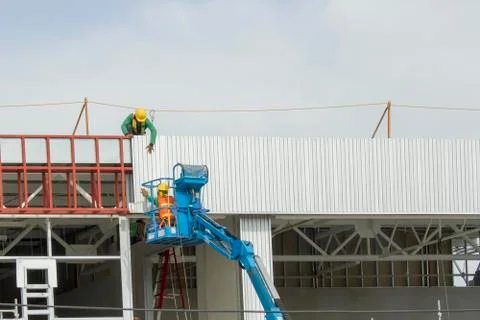 Workers in a baskets are installing sheet, building a factory. Stock Photos