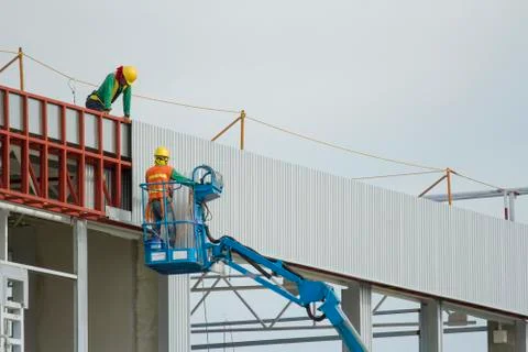 Workers in a baskets are installing sheet, building a factory. Stock Photos